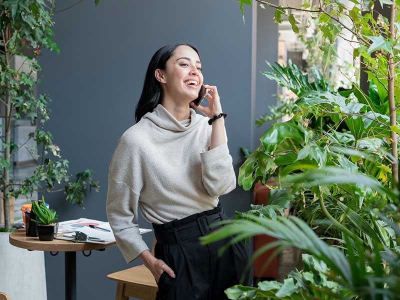 A woman standing near the garden area and smiling while talking on phone