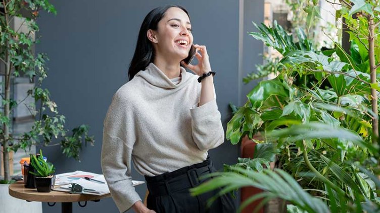 A woman standing near the garden area and smiling while talking on phone