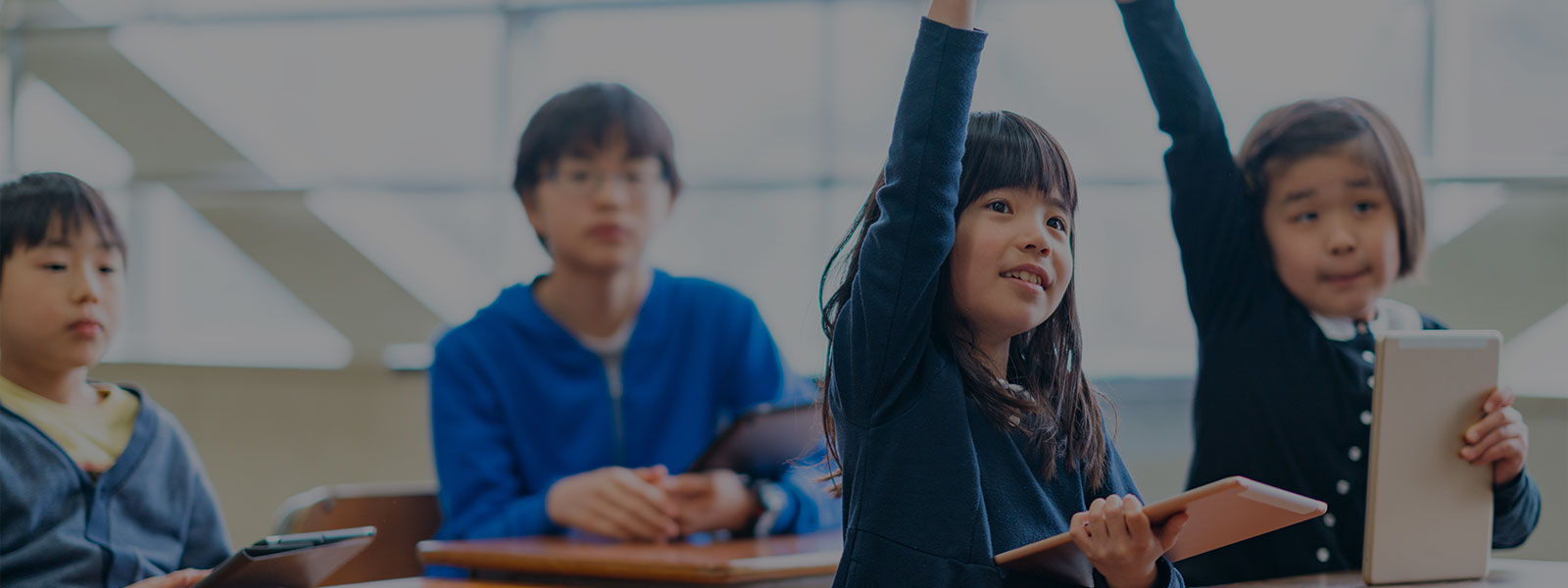 Elementary school children are using digital tablets and studying in a classroom.