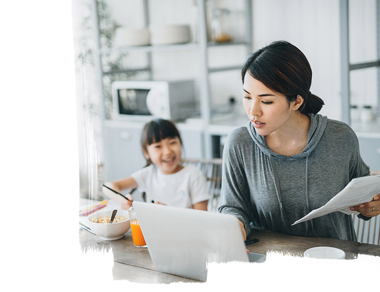 Young Asian mother working from home on a laptop while little daughter is studying from home