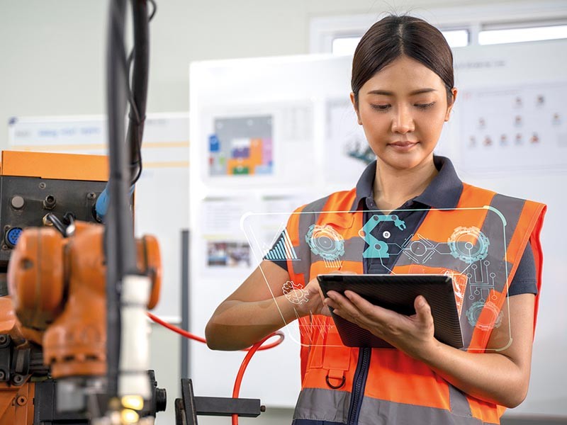 倉庫で、安全なオレンジ色のベストを着用し、自動化技術を示すタブレットを手にする女性