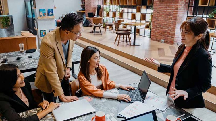 One man and three ladies in a collaborative office space, having a work group discussion 