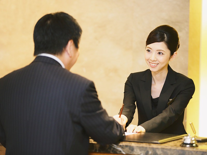 Smiling front-desk lady serving a hotel guest